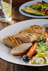 Grilled chicken breast with tabbouleh salad and grilled vegetables on dark wooden background