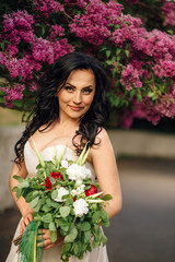young bride in a luxurious dress of flowers is standing in a blooming lilac garden, close up