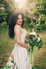 young bride in a luxurious dress of flowers is standing in a blooming lilac garden, close up