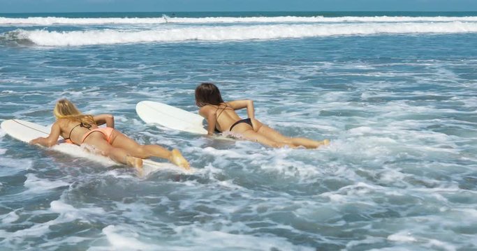 Two girls going into the ocean with their surfboards. Shot taken by a handheld gimbal