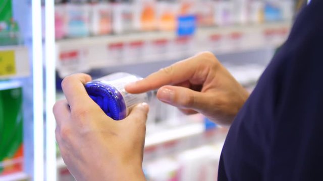 Woman Reading Label On Medicine Bottle Checking Ingredients In Pharmacy