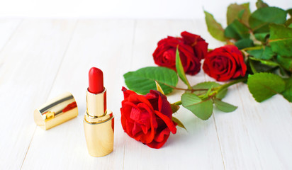 Obraz na płótnie Canvas Red lipstick with red roses on a white wooden background with copy space. Makeup Accessories Selective focus. Various cosmetic products for make-up.