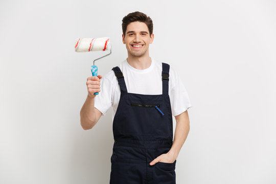 Smiling male builder with arm in pocket holding paint roll