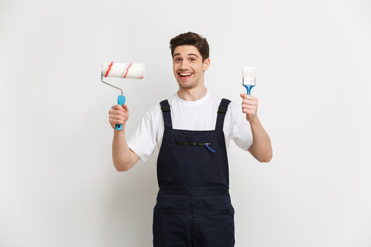 Happy male builder holding paint roll and brush