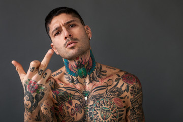 Handsome bare-chested tattooed man making middle finger gesture