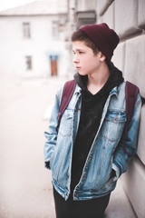 Stylish teen boy 14-16 year old wearing denim jacket, knitted hat and backpack outdoors. Spring...