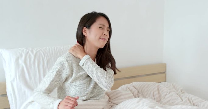 Woman feeling shoulder pain and sitting on bed