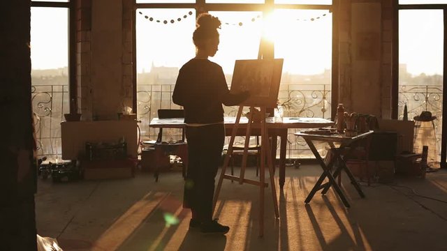 Fully concentrated sophisticated female artist in her 20's is drawing picture on easelin a minimalistic loft styled art studio.