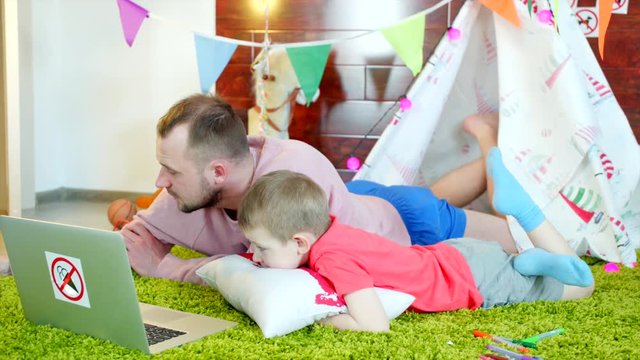Little boy is watching cartoons with his father in the playroom