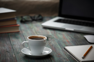 A cup of coffee in the workplace on a wooden table. A cup of coffee in the workplace on a wooden table. The concept of working outside the office