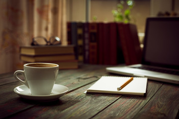 A cup of coffee in the workplace on a wooden table. A cup of coffee in the workplace on a wooden table. The concept of working outside the office