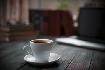 A cup of coffee in the workplace on a wooden table. A cup of coffee in the workplace on a wooden table. The concept of working outside the office