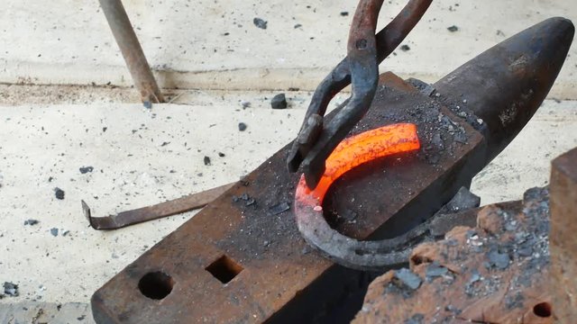 A blacksmith pounding a hammer on red-hot horseshoe on the anvil.