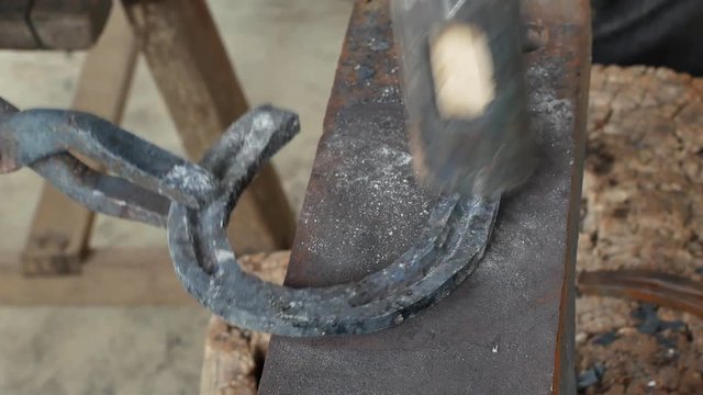 A blacksmith pounding a hammer on red-hot horseshoe on the anvil.
