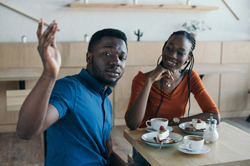african american couple sitting at table with cups of coffee and desserts in cafe