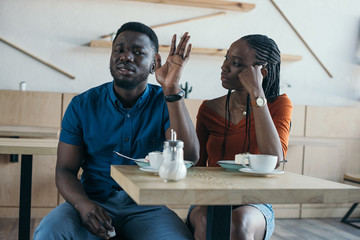 insulted african american man sitting at table with girlfriend in cafe