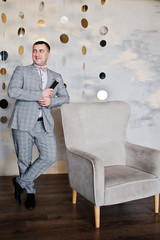 Handsome man in gray suit with microphone against chair background on studio. Toastmaster and showman.