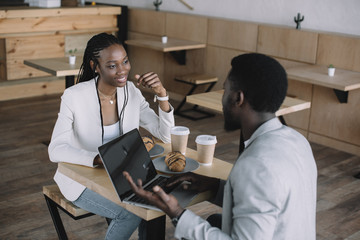 african american friends sitting at table with laptop in coffee shop