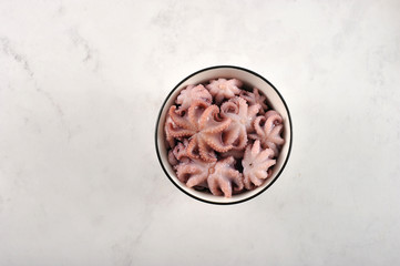 Mini octopus in a round small bowl. Light marble background. View from above. Close-up.