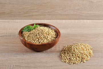 Soy flakes in a round wooden bowl. Near the hill flakes. Soy flakes for addition in minced meat and as a product for vegetarians. Light wooden background. Close-up.