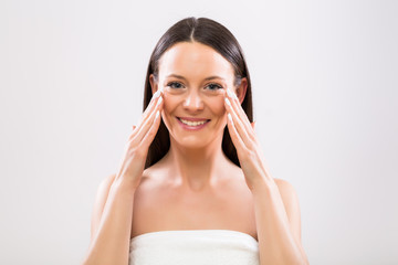 Beautiful woman applying moisturizer on face.