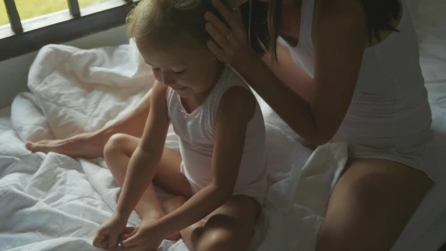 Young mother sits on the bed and combing her daughter in slow motion.