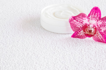 Cream jar and fresh purple orchid flower on the white towel. Natural herbal cream for women. Cares about clean and soft hands, legs, feet and body skin. Healthcare concept. Empty place for text.