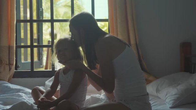 Young mother sits on the bed and combing her daughter in slow motion.