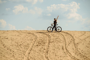 Woman tourist with bicycle at the top of the desert hill at outdoors during a hike in summer