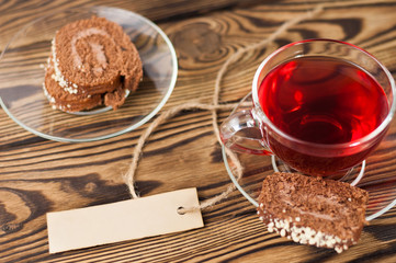 Full cup of red tasty raspberry tea and slice of roll pie and rectangle empty paper attached of rope on old wooden rustic table