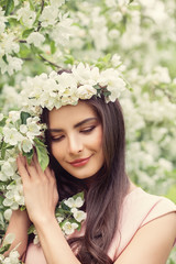 Naklejka premium Beautiful smiling woman with makeup, healthy brown hairstyle and flowers on spring blossom background