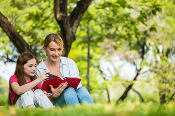 Fototapeta premium Mother and daughter reading a book together in a park. Family, lifestyle and education concept