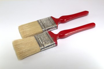 Two paint brushes 2 inches wide with red handles on a wooden background close-up