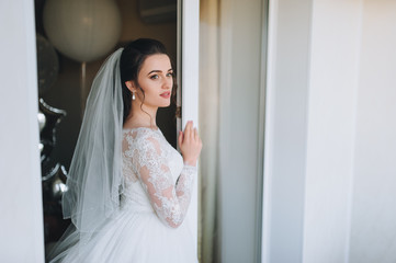 A beautiful bride in a lace dress. She looks out the window. The bride's fees. Waiting for the groom.