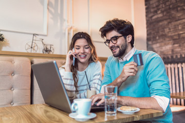 Happy young couple sitting at cafe and shopping online. Woman holding credit card.