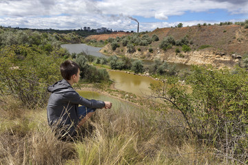 A teenager looks at the landscape of an abandoned sandy quarry on a summer day.
