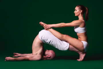Obraz premium Beautiful sporty woman and man in white clothes doing yoga asanas together indoor on green background