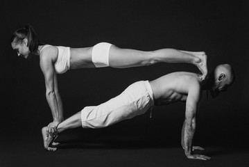 Monochrome portrait of beautiful sporty couple: woman and man in white clothes doing yoga asanas together indoor 