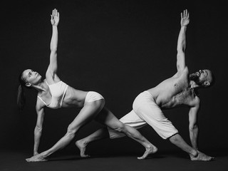 Monochrome portrait of beautiful sporty couple: woman and man in white clothes doing yoga asanas together indoor 
