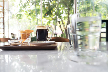 Closeup image of glasses of water and a cup of hot coffee with snack on a wooden tray on the table in cafe