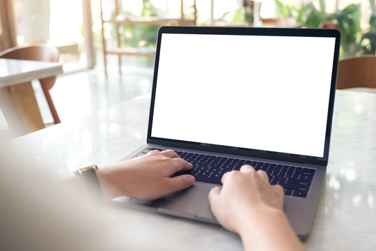 Mockup image of hands using and typing on laptop with blank white desktop screen on table in modern cafe