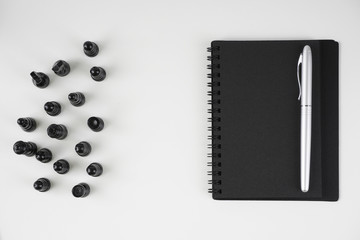 Flat lay image of black book and silver pen over white background