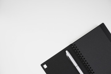 Flat lay image of black book and silver pen over white background
