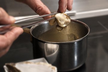 Chef hands pick a freshly cooked oyster out of the pot, copy space