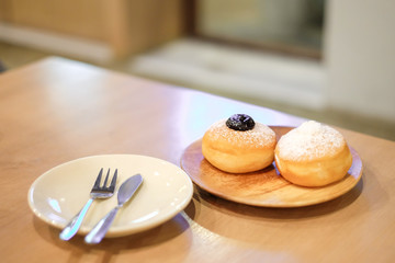 Blueberry Donut and Coconut Donut with powder serve on wooden plate with spoon and fork set on table - Homemade Bakery & Dessert concept.