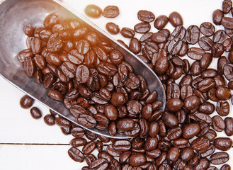 Closeup group of coffee beans put in the stainless spoon,plenty of coffee beans on timber board,warm light tone,blurry light around.