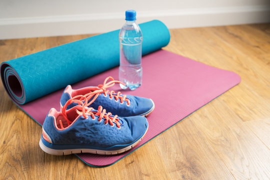 Sport shoes & bottle of water on yoga mat. Healthy lifestyle conceptual. Blue sneakers on a wooden background.