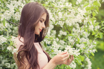 Beautiful woman with long brown hair holding spring apple flowers on floral background