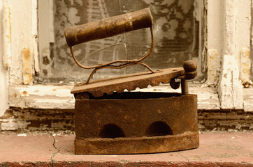 Rusty vintage iron on coals with a slightly opened top cover, standing outside on a windowsill, blurred background: an old window with a wooden frame and broken glass, image in sepia style