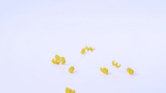 Dry macaroni is strewed on white background in slow motion